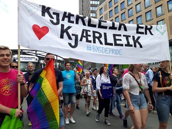 Pride parade. Foran bæres en stor vimpel med teksten "Kjærleik er kjærleik. #Bygdepride"